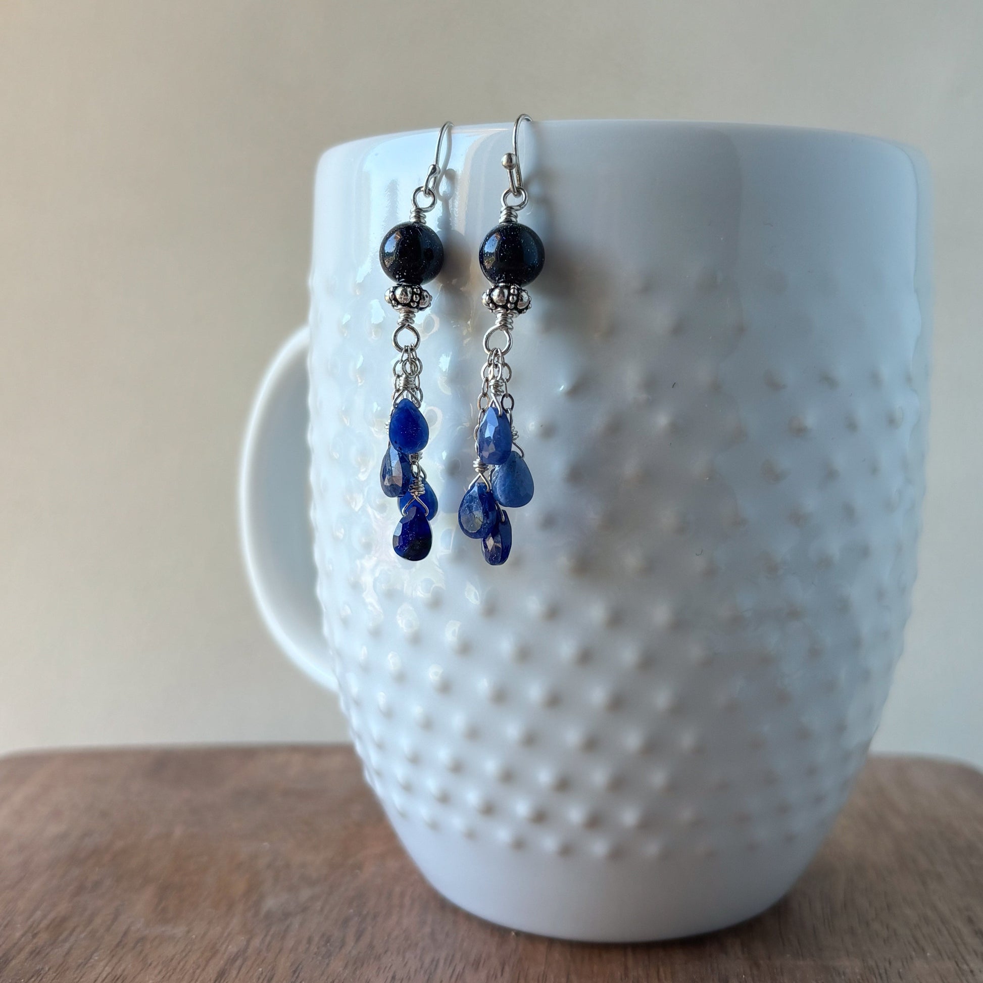 Blue beaded earrings hanging on a white textured mug.