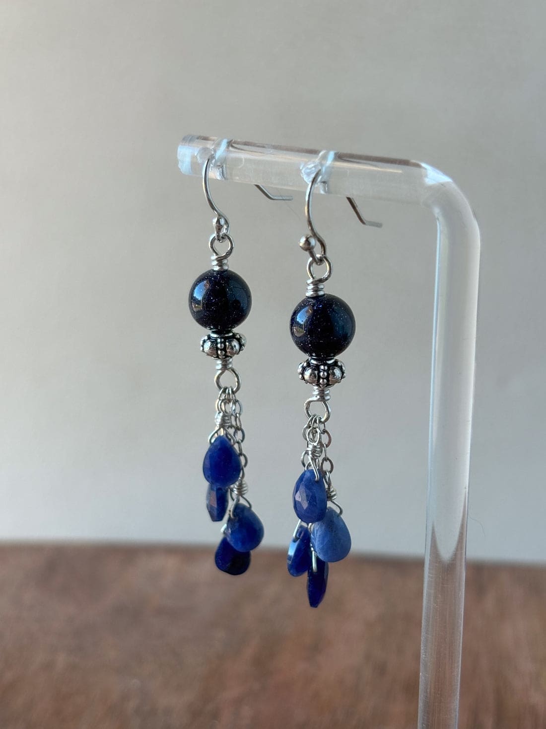 Pair of blue beaded earrings on a clear stand with a neutral background